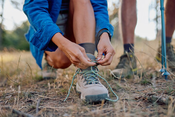 Female hiker tying shoelaces on trekking boots, getting ready for an exciting hike through the beautiful outdoors and lush nature