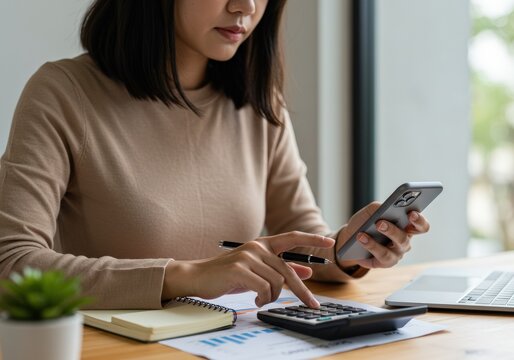 Businesswoman working on financial reports using a calculator and smartphone at her desk.