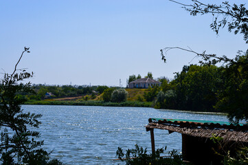 Rustic wooden dock with chairs and a thatched roof by a calm river, surrounded by green forest....