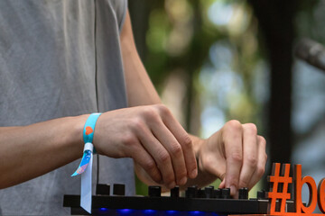 The DJ's hands skillfully control the player, creating music outdoors against backdrop of lush greenery