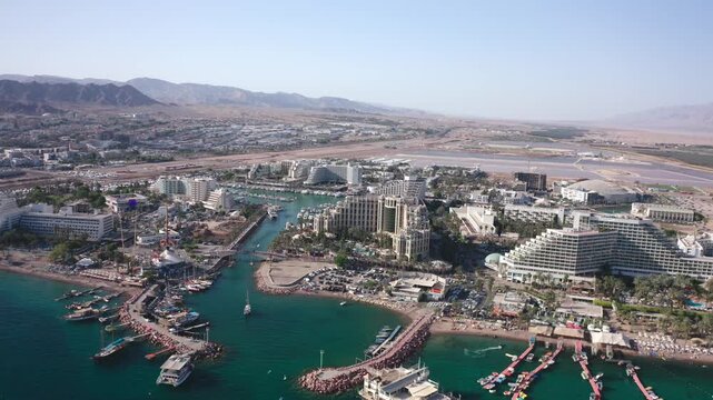 Aerial drone view of Eilat, Israel, showing the coastline with boats, beach, and the iconic bridge, surrounded by the Red Sea&rsquo;s turquoise waters.