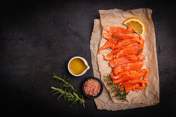 Traditional Norwegian fresh salmon in slices, salted fish or salmon ceviche with lemon and rosemary, top view on black background