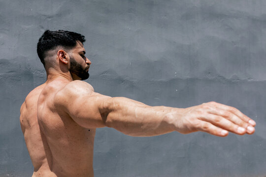 Athletic man with muscular physique stretching outdoors