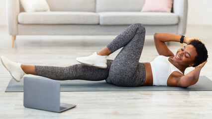 Online Gym. Fit African Lady Doing Abs Exercise At Laptop Lying On Gymnastics Mat Training At Home....