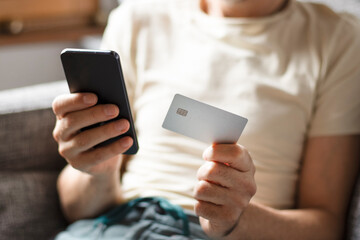Close-Up of Man Holding Credit Card and Smartphone at Home on Sofa