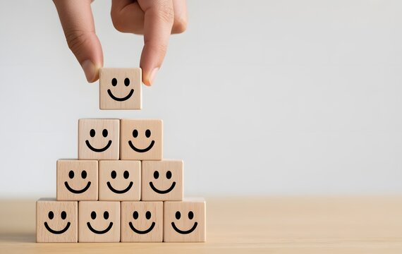 Building Happiness: A hand carefully places a block with a smiley face atop a pyramid of other blocks, symbolizing positive reinforcement and emotional well-being.