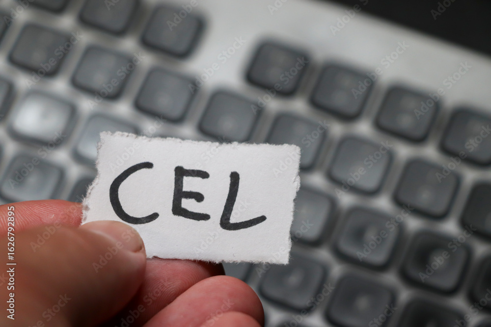 Poster a hand holding a paper with the word cel in focus, set against a blurred keyboard background. this i