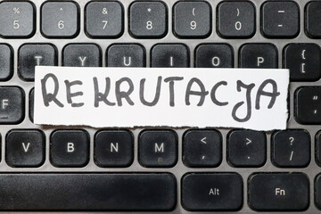 A close-up view of a keyboard featuring a paper note with the word Rekrutacja. The scene highlights...