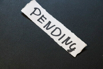 A close-up view of a torn paper label with the word PENDING written in bold letters on a dark...