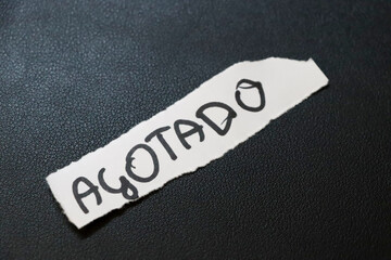 A close-up image of a handwritten note reading Agotado on torn white paper, placed on a textured...