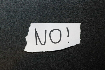 A torn piece of paper with the word NO! written in bold black letters on a textured black...