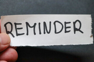 A hand holding a reminder note, emphasizing the importance of tasks. The background is dark,...