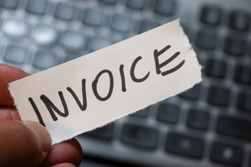 A hand holding a torn piece of paper with the word INVOICE written on it, set against a blurred...