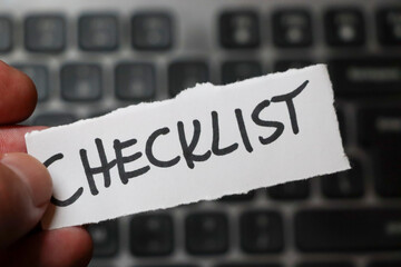 A hand holding a torn paper with the word CHECKLIST written in bold, placed on a blurred background...