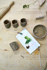 Hand-painted clay napkin rings with botanical imprints in progress. Brushes, paint palette, and...