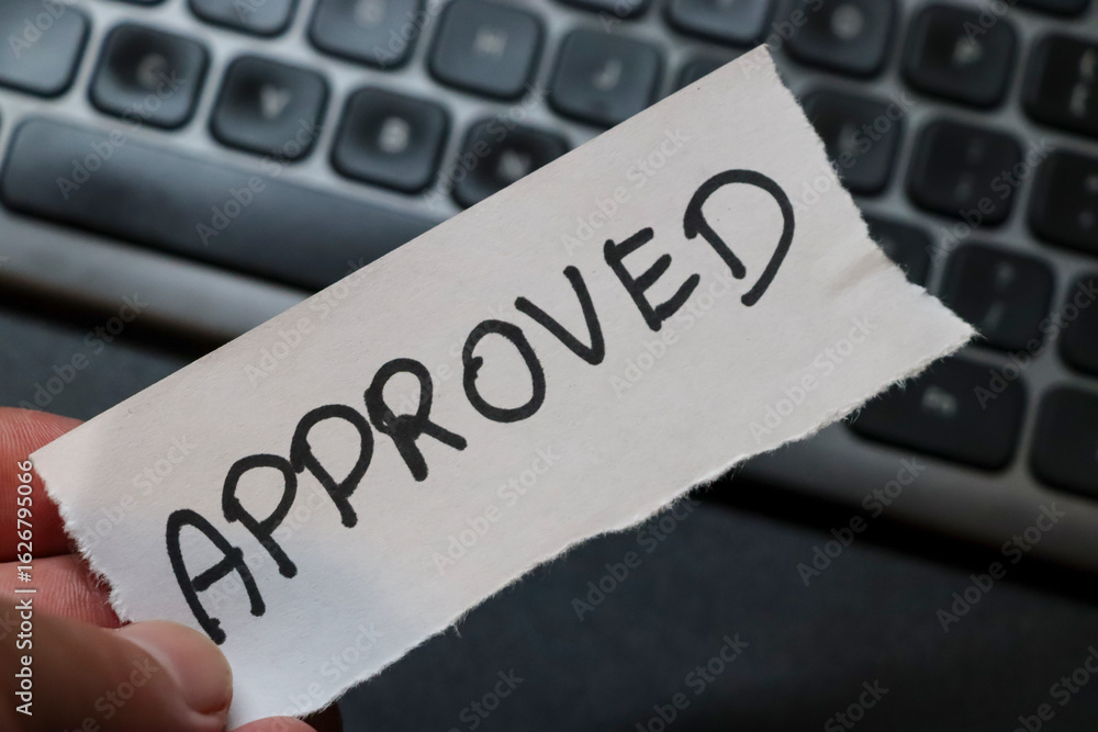 Poster a hand holding an approved note above a computer keyboard, symbolizing successful completion of task
