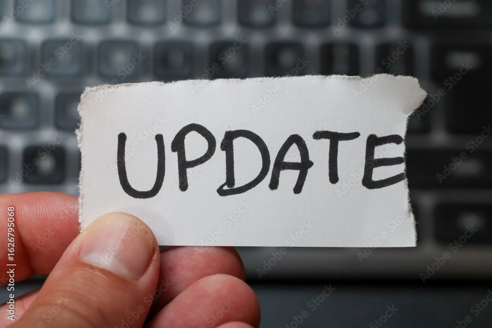 Poster a hand holding a note with the word update against a blurred keyboard background. this image symboli