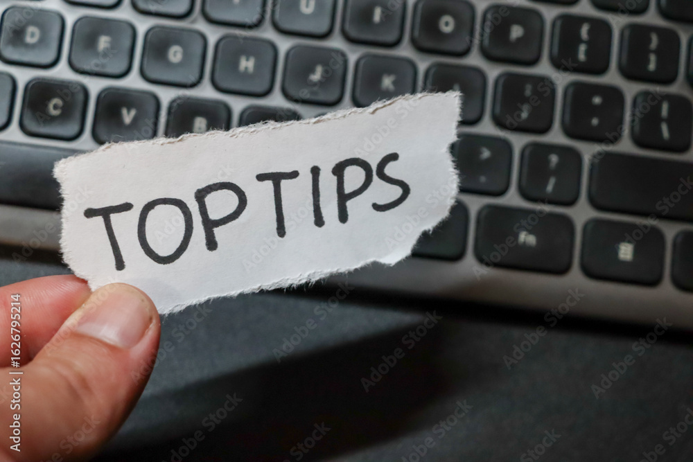Poster close-up of a hand holding a torn paper with the words top tips against a blurred keyboard backgroun