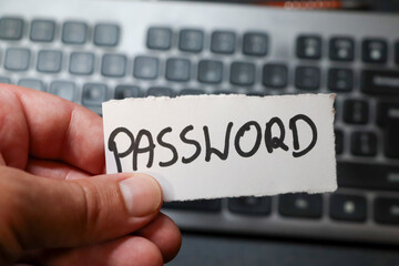 A hand holding a note with the word PASSWORD against a background of a computer keyboard, emphasizing security and digital privacy in modern technology.