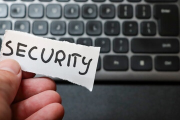 A person holding a torn piece of paper with the word SECURITY against a blurred computer keyboard...