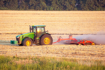 Fototapeta premium Tractor working on agricultural field during sunrise in golden light
