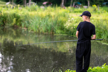 Teen boy fishing on a calm lake during summer day