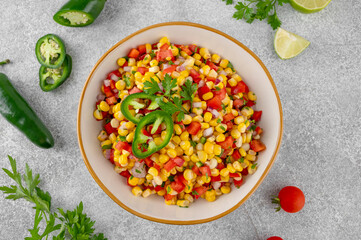 Corn salsa in a bowl with lime, jalapeno pepper, fresh herbs and tortilla chips on a concrete background. Mexican cuisine. Healthy food.