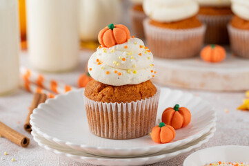 Pumpkin spice cupcakes decorated butter cream frosting, sugar sprinkles and mini sweet pumpkins on top. Thanksgiving or Halloween dessert.
