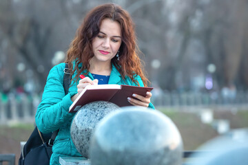 Woman in teal jacket sketches in a notebook near round stone sculptures during daytime