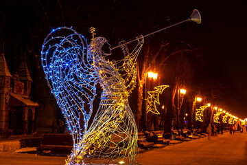 Brightly lit angel sculpture playing trumpet in festive park during winter night