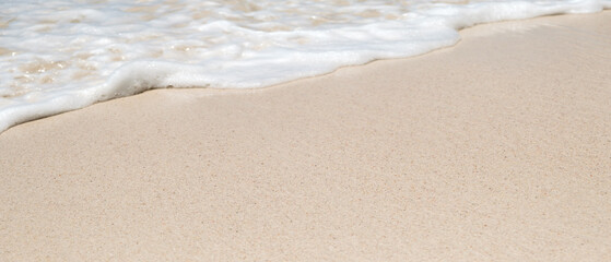 Smooth sandy sea beach with focus on foreground, foamy calm sea water in the background. Vacation concept background.