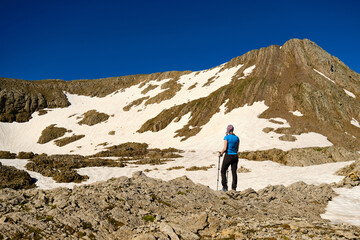 Rear view of a woman with trekking poles resting while climbing a mountain.