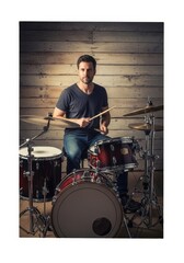 Fototapeta premium Drummer Playing a Drum Kit - A male drummer sits behind his drum kit, holding drumsticks, ready to play. He's wearing a dark shirt and jeans against a wood background