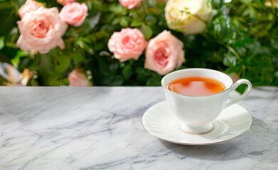 Cup of tea on marble table. Rose garden background. Copy space. Close up.