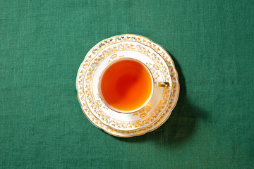 Cup of tea on a saucer and plate. Green textile background. Close up. Top view.