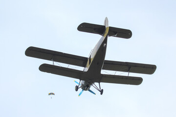 Skydiver descending from a biplane against a clear blue sky at an outdoor event