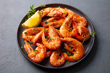 Grilled shrimp with lemon on a black plate. Grey background. Close up.