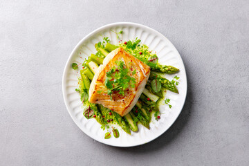 Roasted cod, codfish with asparagus and on plate. Grey background. Close up. Top view.