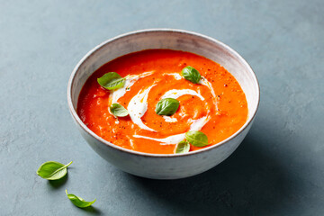Tomato soup with cream and fresh herbs in a bowl. Grey background. Close up.