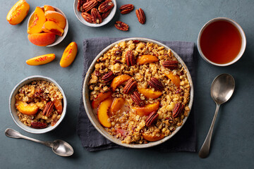 Healthy breakfast concept. Peach crumble cake with pecan nuts in bowl and mug of tea. Grey...