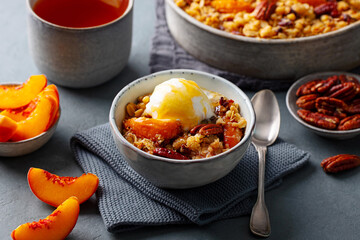Healthy breakfast concept. Peach crumble cake with pecan nuts and vanila ice cream in bowl and mug of tea. Grey background. Close up.