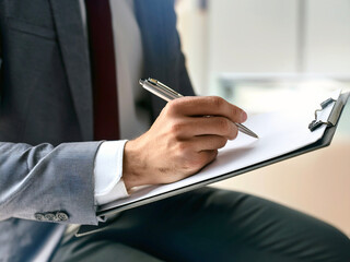 Close up view of a business management consultant taking notes on a clipboard during a meeting