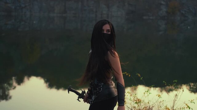 fantasy woman warrior assassin holds dagger in hands. Night dusk view nature river water rocks. sexy girl looking back mystery face hiden mask. Black leather costume, hood. Ninja with sword knife. 4k 