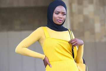 African woman in yellow dress and black hijab confidently posing outdoors
