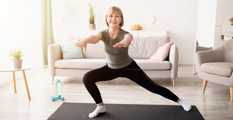 Happy senior lady doing lunges on domestic workout in living room, copy space. Sporty mature woman...