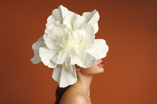 Creative fashion portrait of unrecognizable woman wearing giant white flower headpiece that covers her face, shot against vivid orange background. concept for beauty editorial design