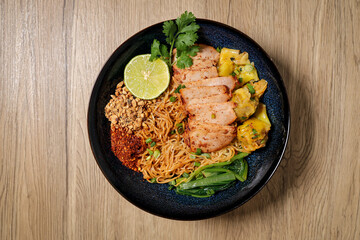 Tom yum egg noodles with bbq pork on wooden background