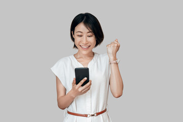 Emotional mature Asian business woman show happiness getting bonus reward or good news on telephone mobile phone. Happy smiling young eastern businesswoman winner showing triumph yes gesture isolated