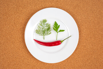 Bright red chili pepper and fresh green herbs arranged on a white plate for culinary art