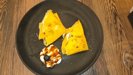 Delicious crepes with cream garnish and blueberry on elegant black plate. Chestnut pancakes with...